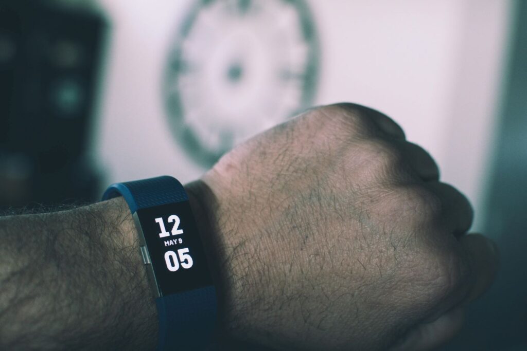 Blue Fitbit Charge Displaying 12:05 May 9
